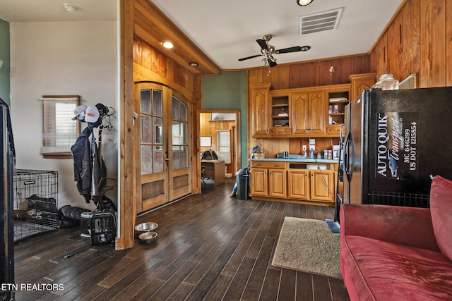 kitchen with wood walls, black refrigerator, ceiling fan, and dark hardwood / wood-style floors