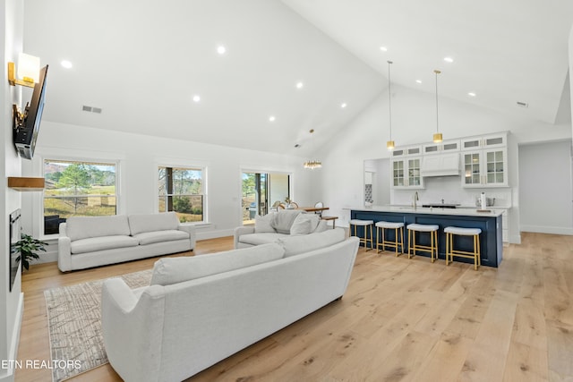 living room featuring sink, high vaulted ceiling, and light hardwood / wood-style flooring