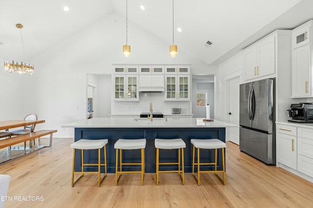 kitchen with a kitchen island with sink, white cabinets, stainless steel fridge, decorative light fixtures, and light hardwood / wood-style floors