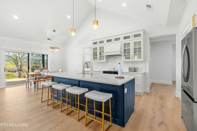 kitchen featuring stainless steel fridge, pendant lighting, a center island with sink, light hardwood / wood-style flooring, and white cabinetry