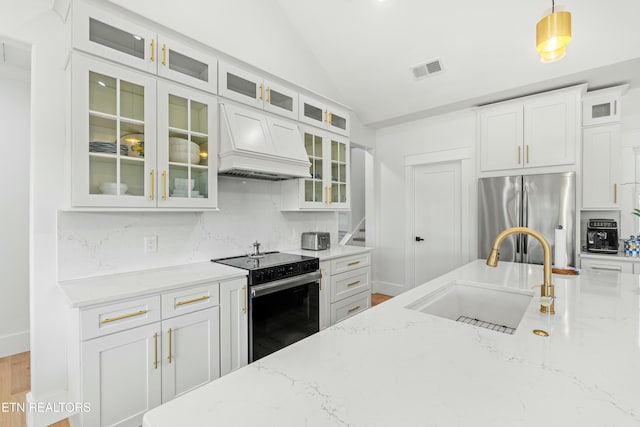 kitchen with pendant lighting, sink, light stone countertops, appliances with stainless steel finishes, and custom range hood