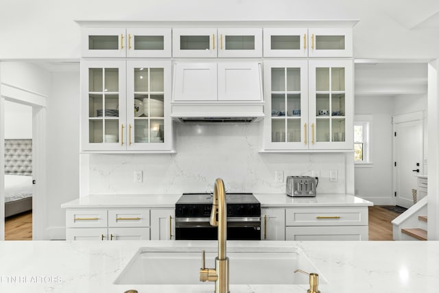 kitchen featuring white cabinets, light wood-type flooring, stainless steel stove, and light stone countertops