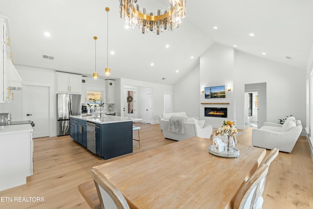 dining space featuring high vaulted ceiling, light hardwood / wood-style flooring, a notable chandelier, and sink