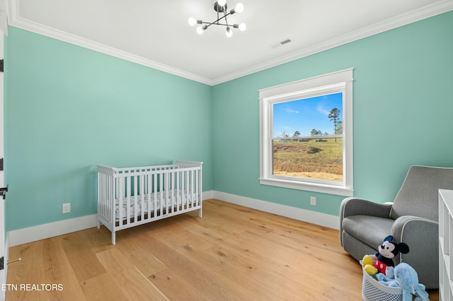 bedroom featuring light hardwood / wood-style flooring, a chandelier, a crib, and ornamental molding