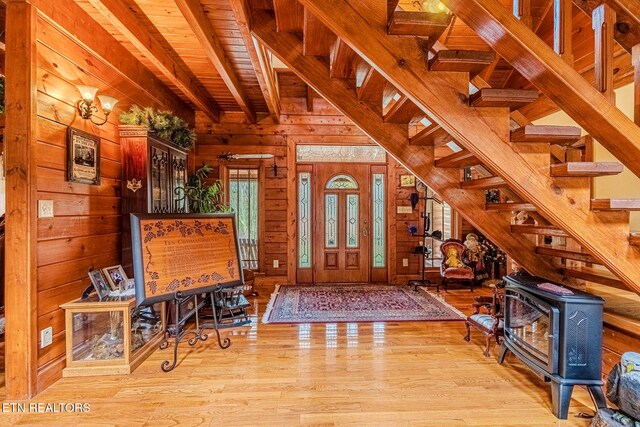 foyer entrance with wooden walls, light hardwood / wood-style flooring, wooden ceiling, beamed ceiling, and a wood stove