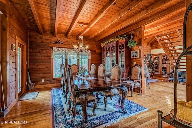 unfurnished dining area with wooden walls, light hardwood / wood-style flooring, beamed ceiling, and a notable chandelier