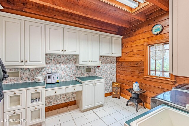 kitchen with beam ceiling, wood walls, white cabinets, and light tile patterned floors