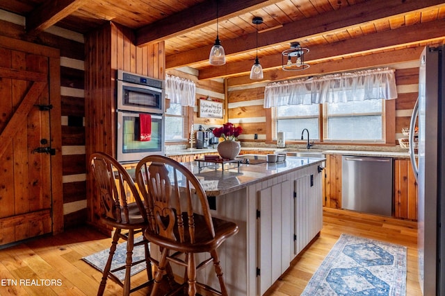 kitchen featuring appliances with stainless steel finishes, light stone counters, wooden walls, light hardwood / wood-style flooring, and beamed ceiling