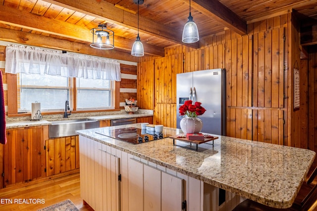 kitchen with sink, wooden walls, appliances with stainless steel finishes, beamed ceiling, and light stone counters