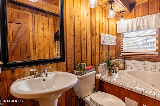 bathroom with a bath, sink, toilet, and wood walls