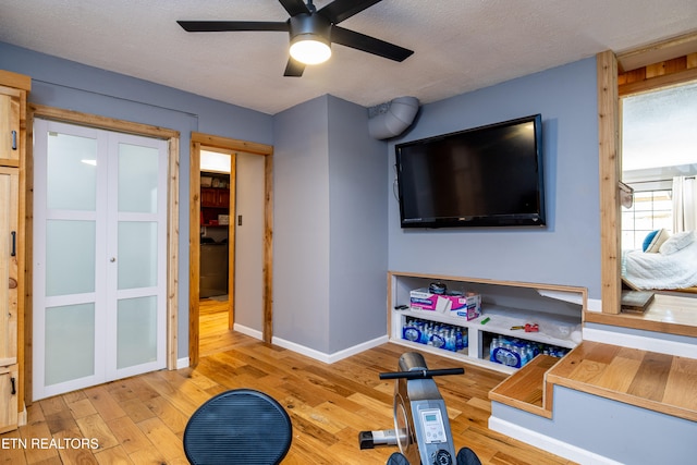 exercise room with ceiling fan, light hardwood / wood-style flooring, and a textured ceiling