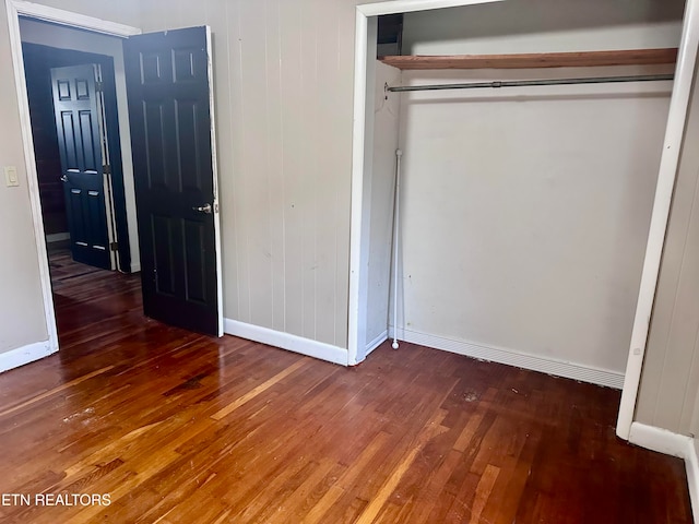 unfurnished bedroom with dark hardwood / wood-style flooring, a closet, and wood walls