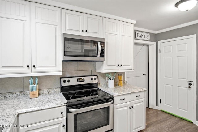 kitchen with wood-type flooring, stainless steel appliances, white cabinetry, and tasteful backsplash