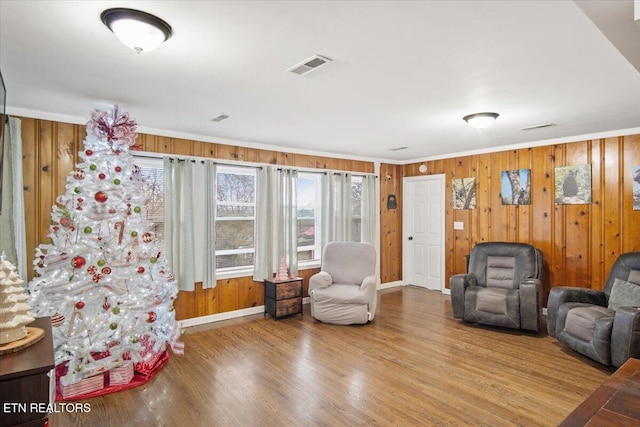 living room with hardwood / wood-style flooring, wood walls, and ornamental molding