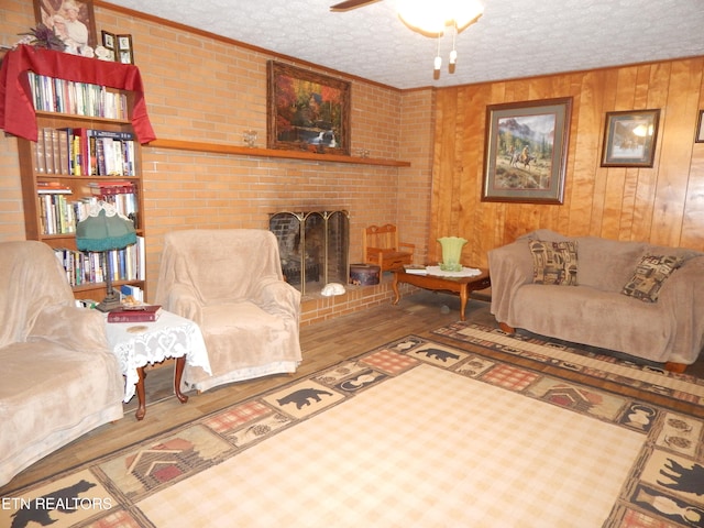 living room featuring a brick fireplace, hardwood / wood-style flooring, ceiling fan, a textured ceiling, and brick wall