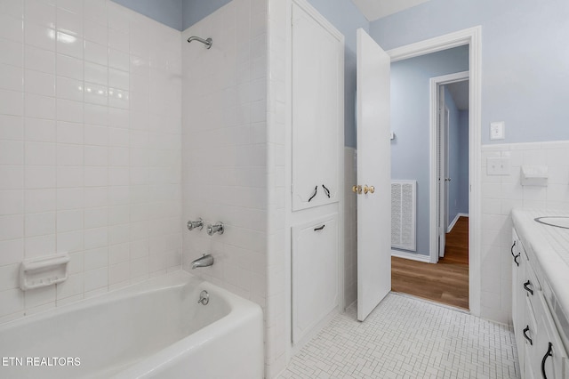 bathroom with hardwood / wood-style floors, vanity, tile walls, and tiled shower / bath