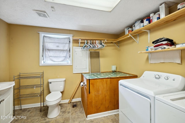 laundry area featuring electric panel, washer and clothes dryer, light tile patterned flooring, and a textured ceiling