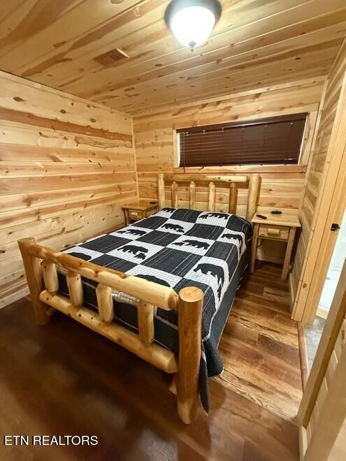 bedroom with dark hardwood / wood-style flooring, wooden walls, and wooden ceiling