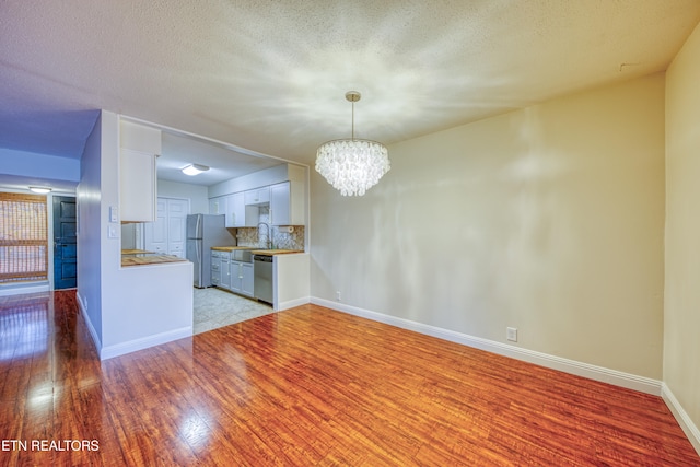 interior space with stainless steel appliances, backsplash, a textured ceiling, white cabinets, and light wood-type flooring