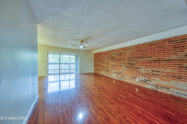 empty room featuring wood-type flooring, a textured ceiling, ceiling fan, and brick wall