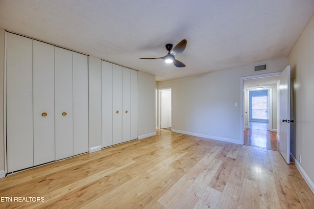 unfurnished bedroom with a textured ceiling, light hardwood / wood-style flooring, ceiling fan, and multiple closets