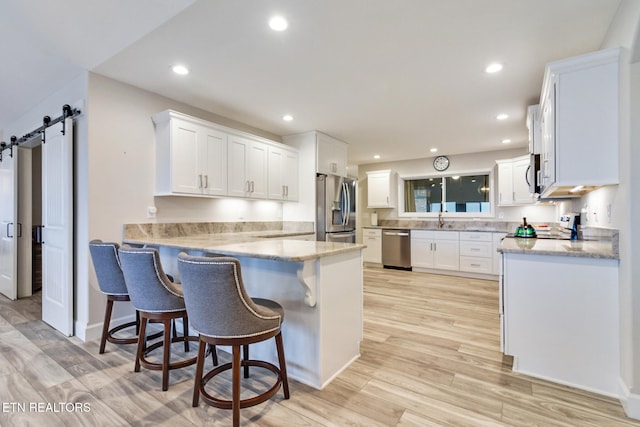 kitchen with a barn door, white cabinets, light hardwood / wood-style floors, and appliances with stainless steel finishes