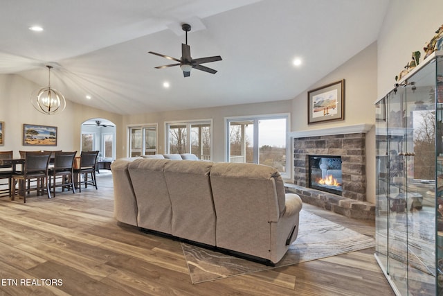 living room featuring a stone fireplace, high vaulted ceiling, wood-type flooring, and ceiling fan with notable chandelier