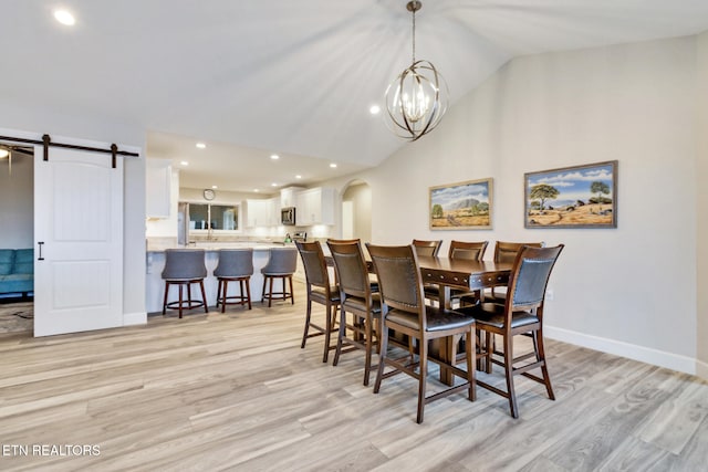 dining area with a notable chandelier, a barn door, vaulted ceiling, and light hardwood / wood-style flooring