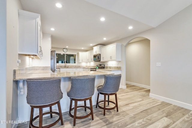 kitchen with kitchen peninsula, light wood-type flooring, a breakfast bar, white cabinets, and appliances with stainless steel finishes