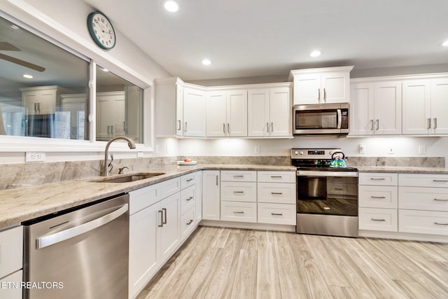 kitchen with sink, light stone counters, light hardwood / wood-style floors, white cabinets, and appliances with stainless steel finishes