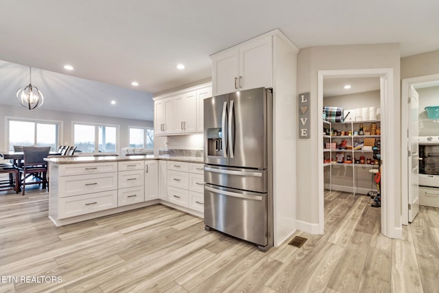 kitchen featuring white cabinetry, kitchen peninsula, stainless steel fridge, light hardwood / wood-style floors, and decorative light fixtures