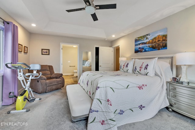 bedroom with carpet, a tray ceiling, ensuite bath, and ceiling fan