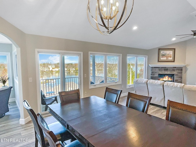 dining space featuring lofted ceiling, ceiling fan with notable chandelier, a water view, light wood-type flooring, and a fireplace