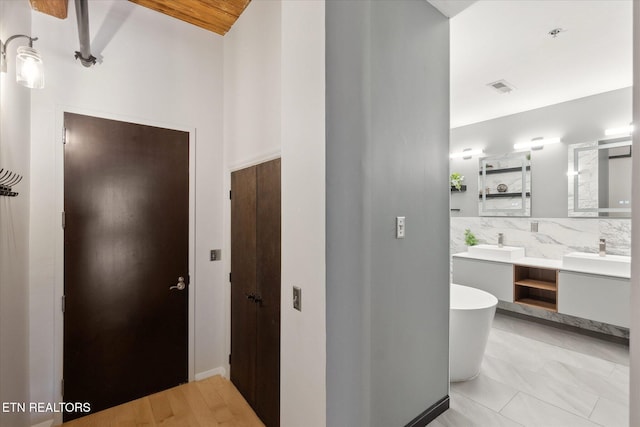 bathroom featuring a tub to relax in, decorative backsplash, vanity, and wood-type flooring