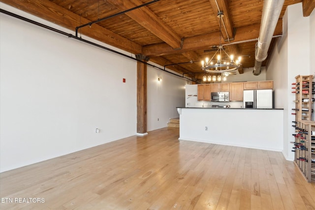 unfurnished living room with beam ceiling, an inviting chandelier, light wood-type flooring, and wooden ceiling