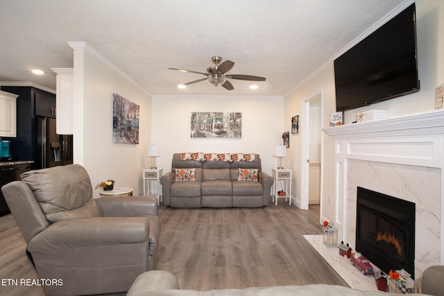 living room featuring light wood-type flooring, ceiling fan, crown molding, and a tiled fireplace