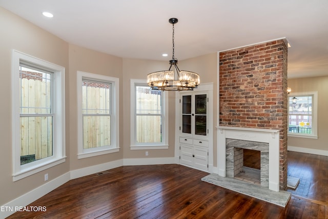 unfurnished dining area with a notable chandelier, a fireplace, and dark hardwood / wood-style floors