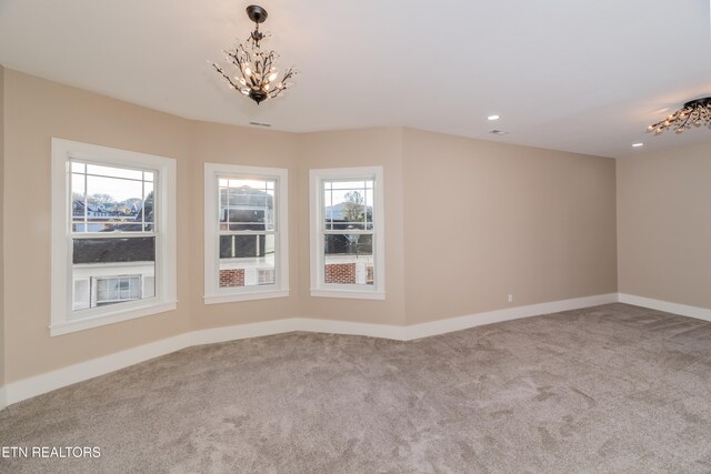 carpeted spare room with an inviting chandelier