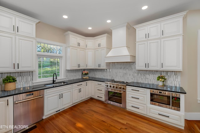 kitchen with white cabinetry, appliances with stainless steel finishes, sink, and custom range hood