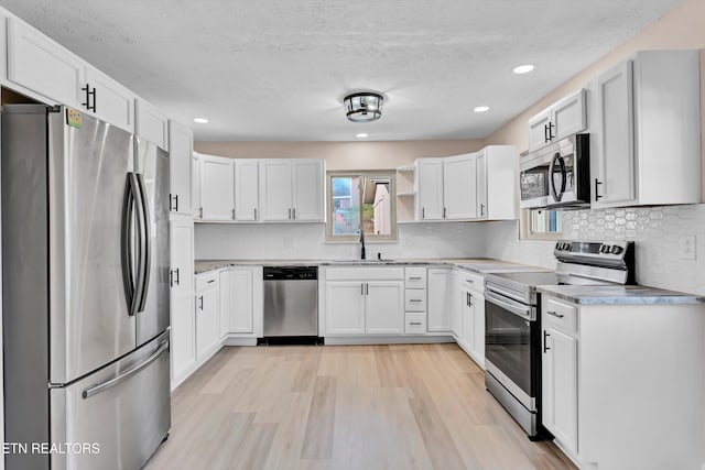 kitchen with sink, appliances with stainless steel finishes, a textured ceiling, white cabinets, and light wood-type flooring