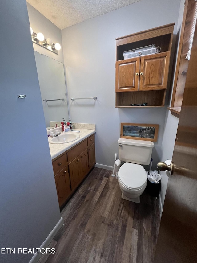 bathroom with hardwood / wood-style flooring, vanity, toilet, and a textured ceiling