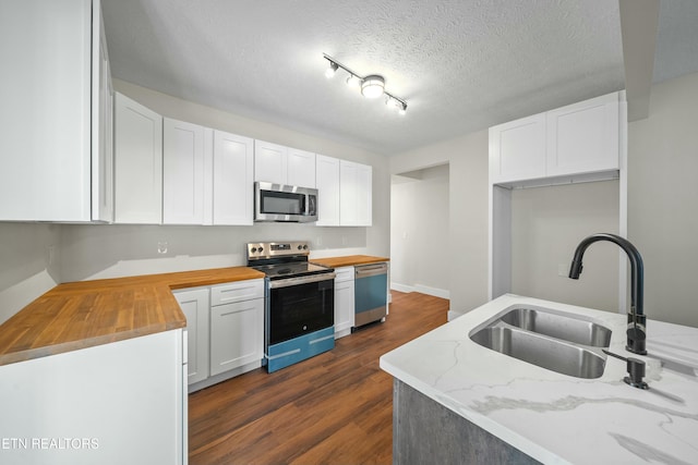 kitchen with butcher block counters, sink, dark wood-type flooring, white cabinets, and appliances with stainless steel finishes