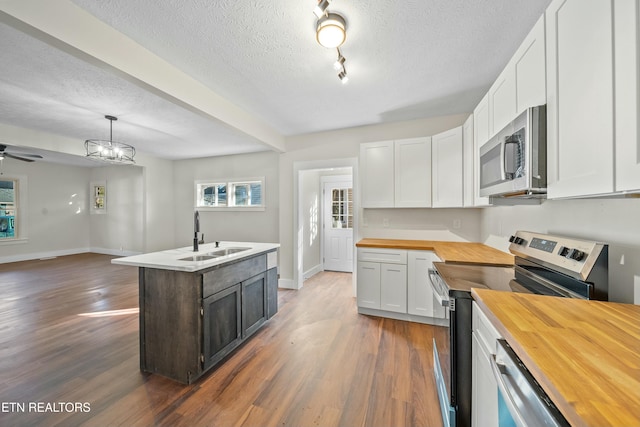 kitchen featuring wood counters, stainless steel appliances, sink, pendant lighting, and white cabinetry