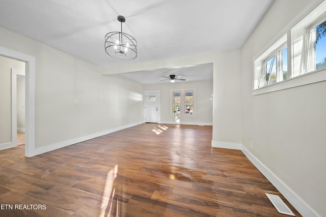 unfurnished living room with dark hardwood / wood-style flooring, plenty of natural light, and ceiling fan with notable chandelier