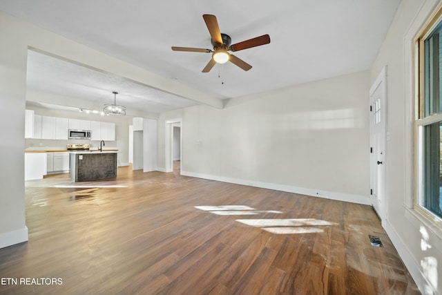 unfurnished living room featuring hardwood / wood-style floors, beamed ceiling, ceiling fan with notable chandelier, and sink