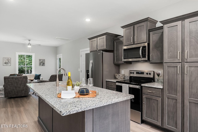 kitchen featuring light stone countertops, an island with sink, stainless steel appliances, and light wood-type flooring