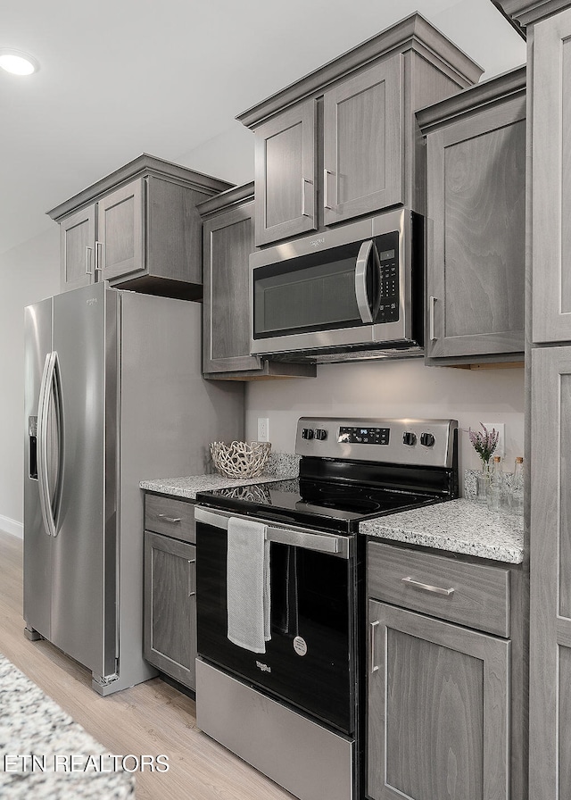 kitchen with light stone countertops, stainless steel appliances, light hardwood / wood-style flooring, and gray cabinetry