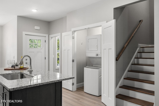 kitchen featuring stacked washer / dryer, light stone counters, sink, and light wood-type flooring