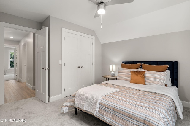 bedroom with ceiling fan, a closet, light colored carpet, and vaulted ceiling