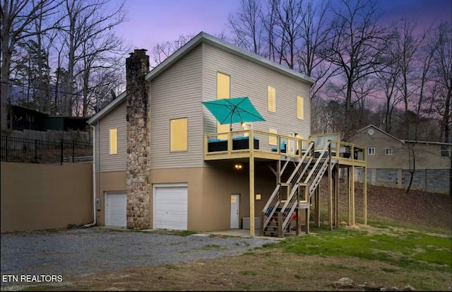 back house at dusk featuring a garage and a deck